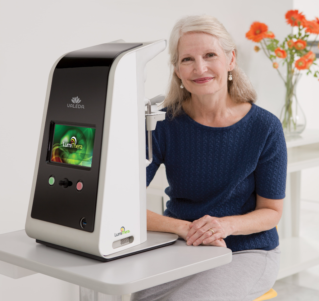 A patient sitting with a LumiThera Valeda device
